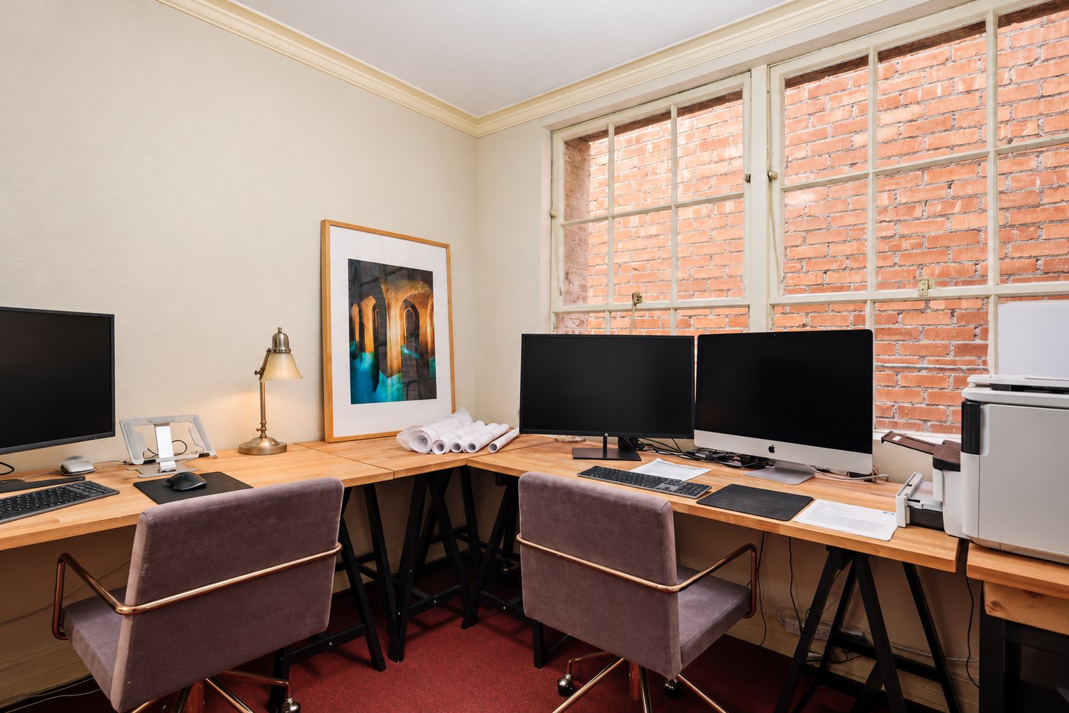 Two workstations along wood desks beside the window